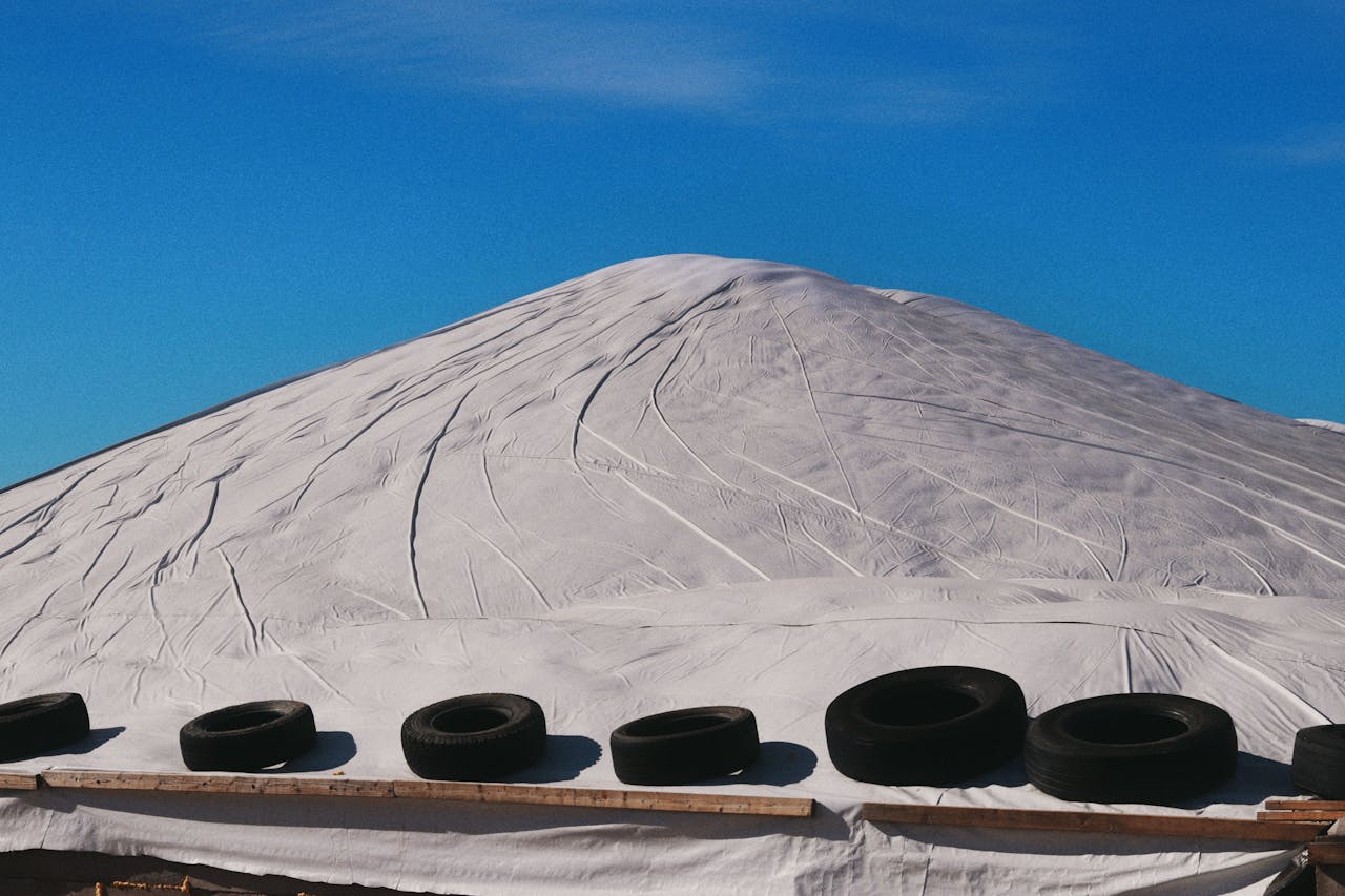 White silage cover topped with tires under a clear blue sky.